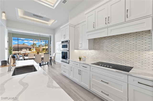 kitchen featuring sink, light hardwood / wood-style flooring, decorative backsplash, light stone counters, and white cabinetry