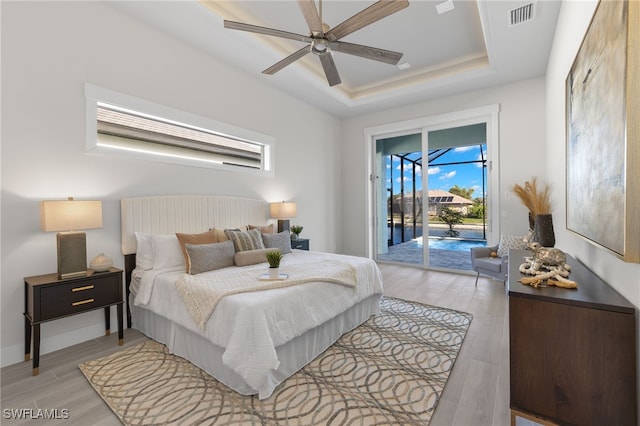 bedroom featuring a raised ceiling, access to exterior, ceiling fan, and light hardwood / wood-style flooring