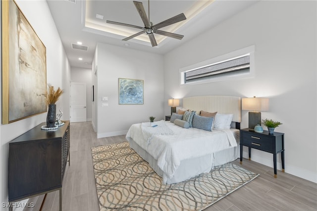 bedroom with ceiling fan, a raised ceiling, and light wood-type flooring