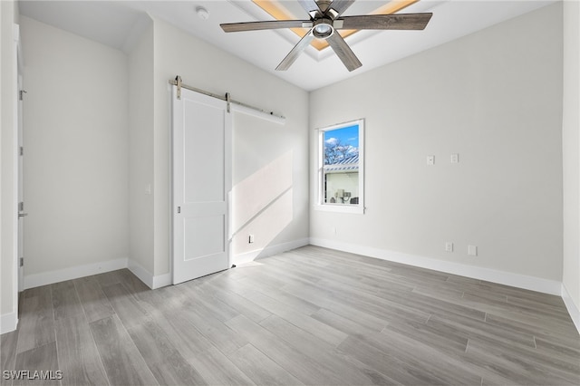 unfurnished bedroom with light wood-type flooring, a barn door, and ceiling fan