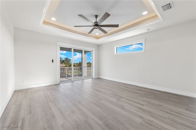 empty room featuring a tray ceiling, ceiling fan, and light hardwood / wood-style floors