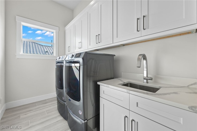 clothes washing area featuring separate washer and dryer, sink, cabinets, and light hardwood / wood-style floors