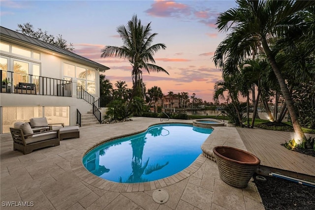 pool at dusk featuring a deck, an in ground hot tub, and a patio