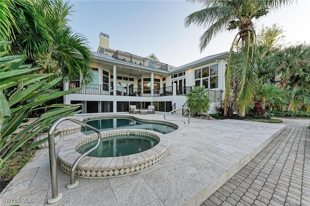 back of property with an in ground hot tub, a balcony, ceiling fan, and a patio area