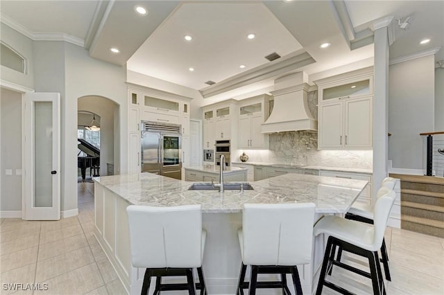 kitchen with sink, built in refrigerator, a spacious island, decorative backsplash, and custom range hood