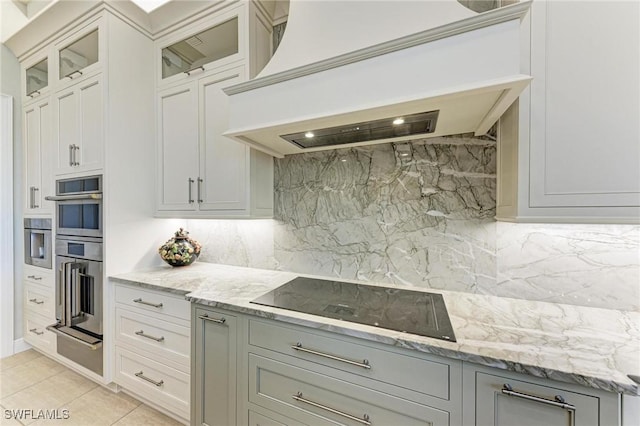 kitchen featuring custom range hood, backsplash, light tile patterned floors, and black electric stovetop