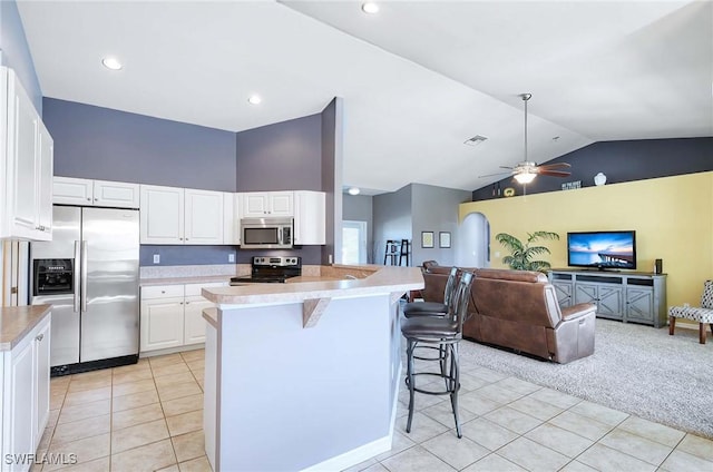 kitchen featuring a breakfast bar, lofted ceiling, light carpet, white cabinets, and appliances with stainless steel finishes