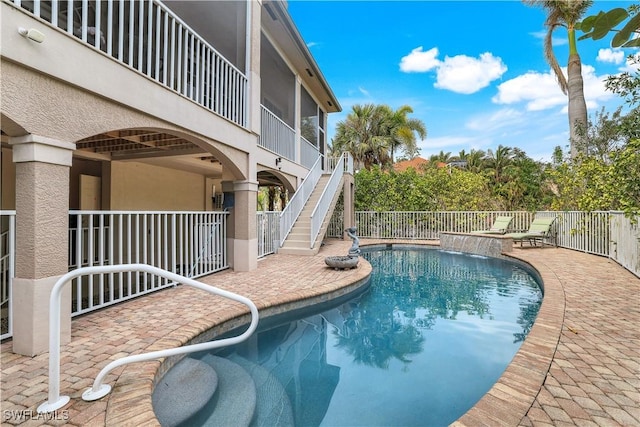 view of swimming pool with pool water feature, a sunroom, and a patio