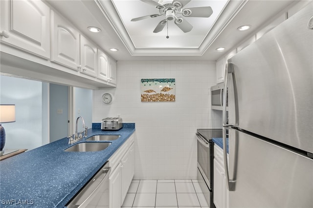 kitchen with stainless steel appliances, a tray ceiling, sink, light tile patterned floors, and white cabinets