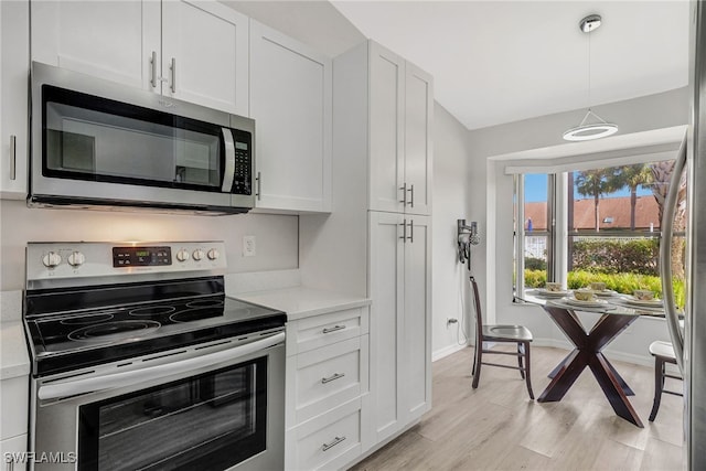 kitchen featuring light wood-type flooring, white cabinetry, stainless steel appliances, and hanging light fixtures