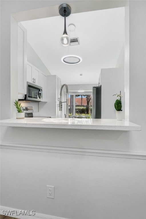 kitchen with kitchen peninsula, vaulted ceiling, stainless steel appliances, and white cabinetry