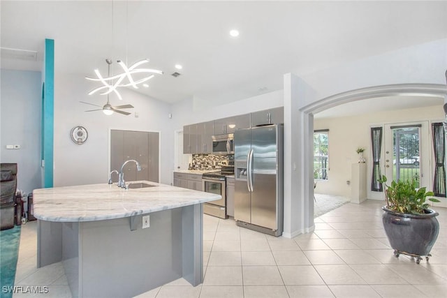 kitchen with gray cabinetry, sink, hanging light fixtures, light stone counters, and stainless steel appliances