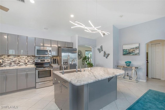 kitchen featuring appliances with stainless steel finishes, gray cabinetry, sink, decorative light fixtures, and an island with sink