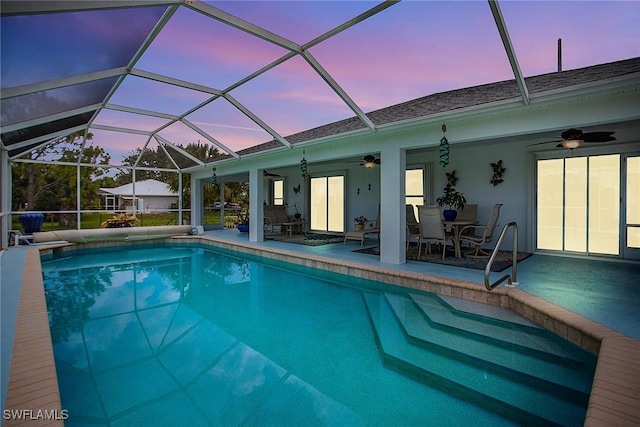 pool at dusk featuring a lanai, ceiling fan, and a patio