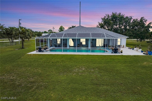 back house at dusk featuring a yard and glass enclosure