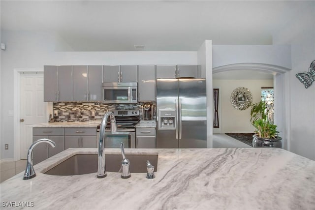 kitchen featuring gray cabinets, light stone counters, sink, and appliances with stainless steel finishes