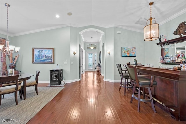 dining space with bar area, hardwood / wood-style flooring, an inviting chandelier, and ornamental molding