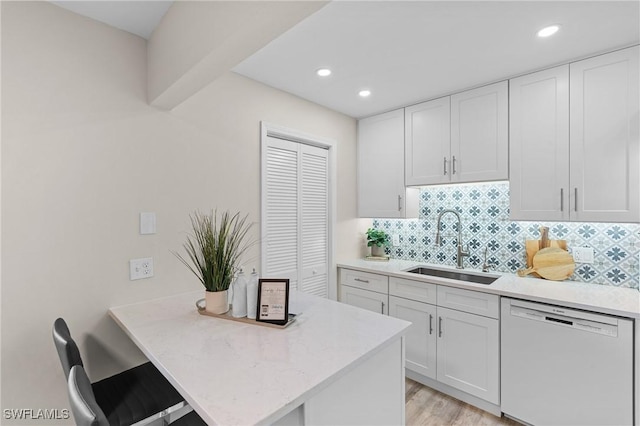 kitchen featuring white cabinets, tasteful backsplash, sink, light hardwood / wood-style flooring, and dishwasher