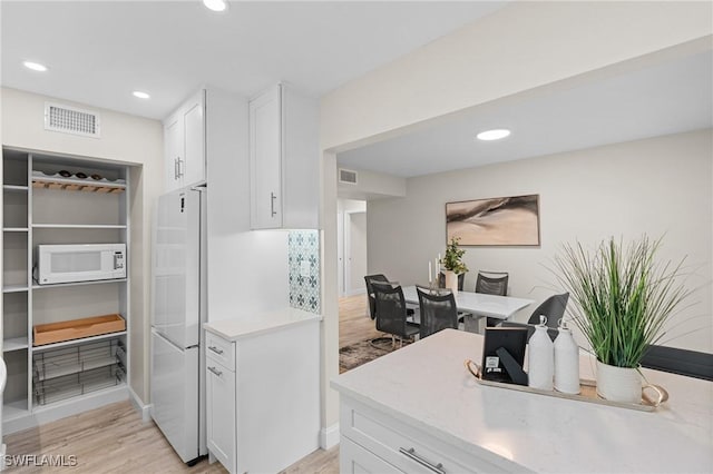 kitchen with white cabinetry, white appliances, and light hardwood / wood-style flooring