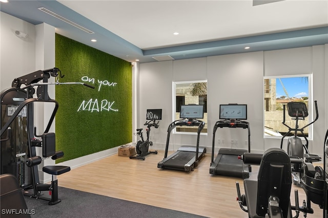 exercise room with an accent wall, recessed lighting, baseboards, and wood finished floors