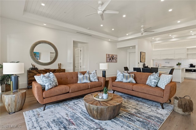 living area featuring recessed lighting, a raised ceiling, and light wood finished floors