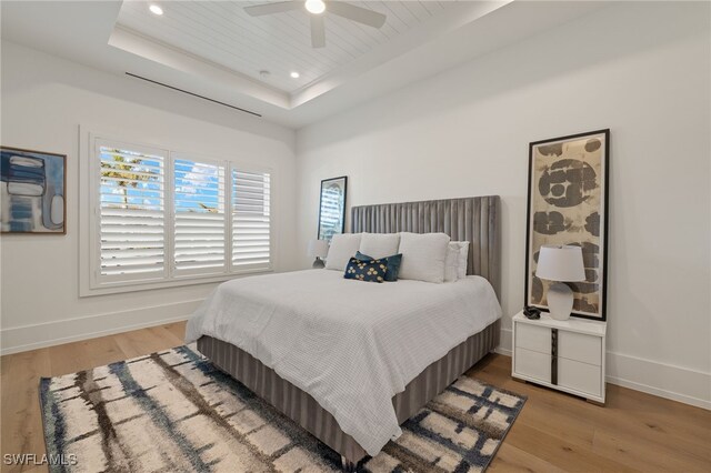 bedroom featuring recessed lighting, a raised ceiling, baseboards, and wood finished floors