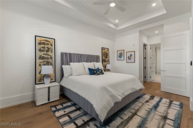 bedroom featuring wood finished floors, recessed lighting, a raised ceiling, and baseboards