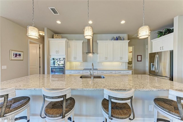 kitchen with pendant lighting, sink, appliances with stainless steel finishes, white cabinetry, and a center island with sink