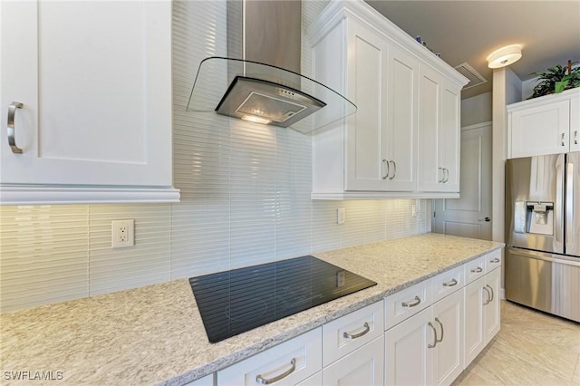 kitchen with white cabinets, black electric stovetop, wall chimney range hood, and stainless steel fridge