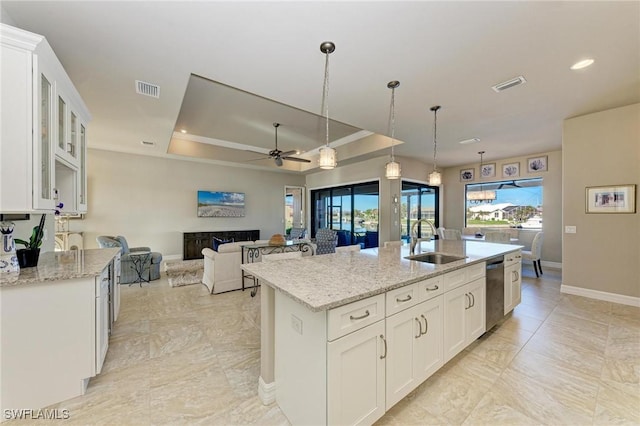 kitchen with sink, white cabinetry, decorative light fixtures, a center island with sink, and a tray ceiling