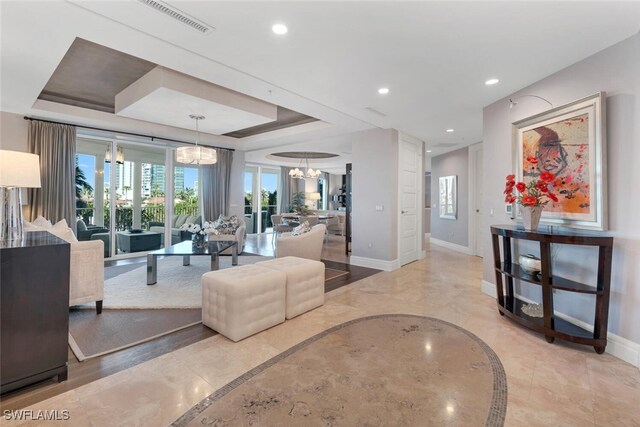 living room featuring plenty of natural light, a raised ceiling, and a chandelier