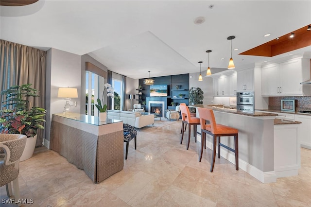 kitchen with white cabinetry, a kitchen breakfast bar, open floor plan, a lit fireplace, and backsplash