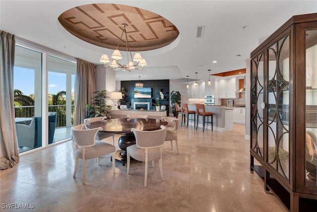 dining space with an inviting chandelier, a lit fireplace, visible vents, and a raised ceiling