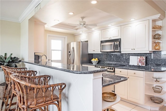 kitchen featuring white cabinetry, stainless steel appliances, a kitchen breakfast bar, kitchen peninsula, and a tray ceiling