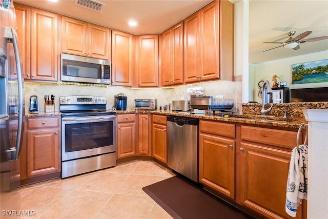 kitchen with sink, stainless steel appliances, ornamental molding, and dark stone countertops