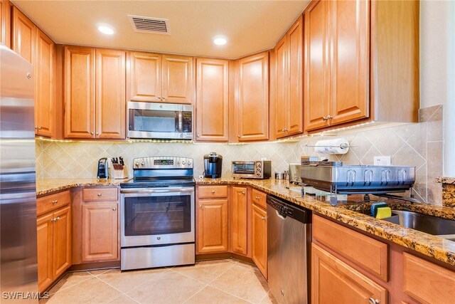 kitchen with backsplash, stainless steel appliances, light stone counters, and light tile patterned flooring