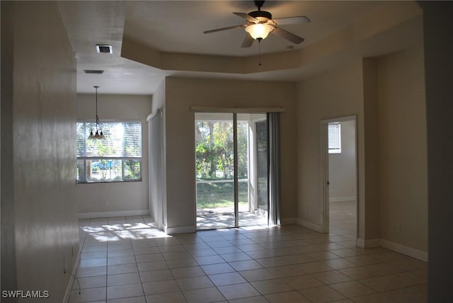 unfurnished room featuring a tray ceiling, light tile patterned flooring, and ceiling fan with notable chandelier