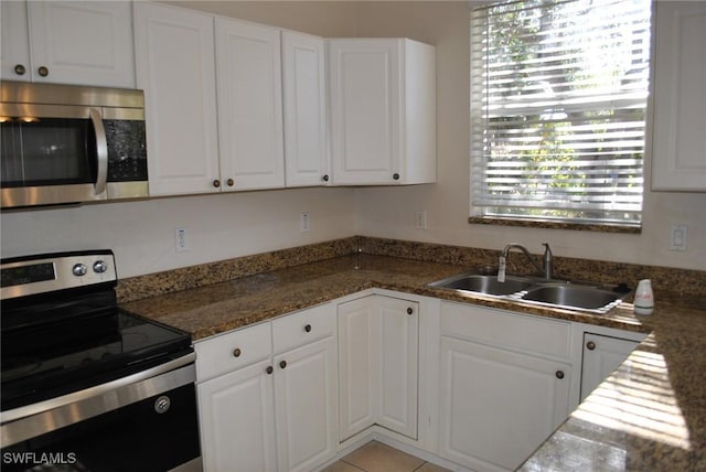 kitchen featuring sink, light tile patterned floors, dark stone counters, white cabinets, and appliances with stainless steel finishes