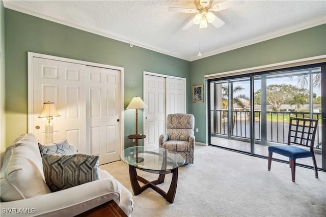 living area featuring light carpet, ceiling fan, a textured ceiling, and ornamental molding