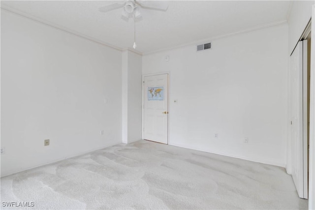 spare room featuring crown molding, light colored carpet, visible vents, and ceiling fan