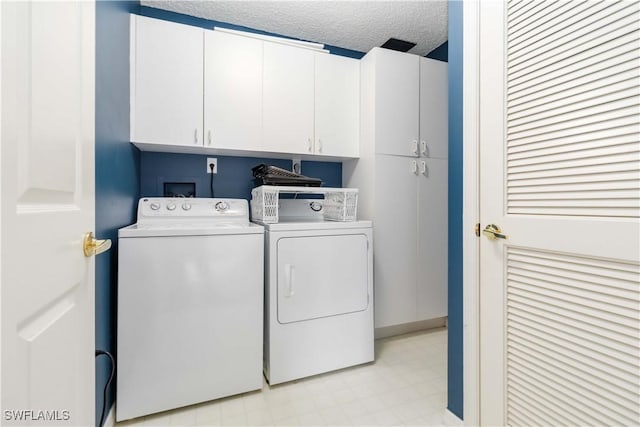 laundry room with washing machine and dryer, cabinet space, light floors, and a textured ceiling