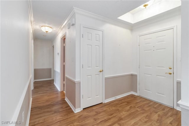 hallway featuring a skylight, baseboards, ornamental molding, and light wood finished floors