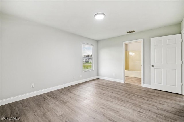 unfurnished bedroom with ensuite bathroom and wood-type flooring