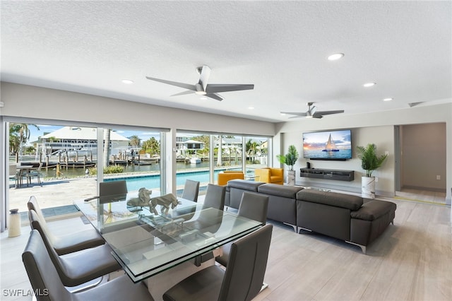 dining space featuring ceiling fan, a water view, a textured ceiling, and light wood-type flooring