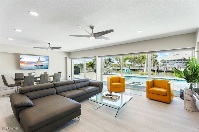 living room featuring ceiling fan, light hardwood / wood-style floors, and a textured ceiling