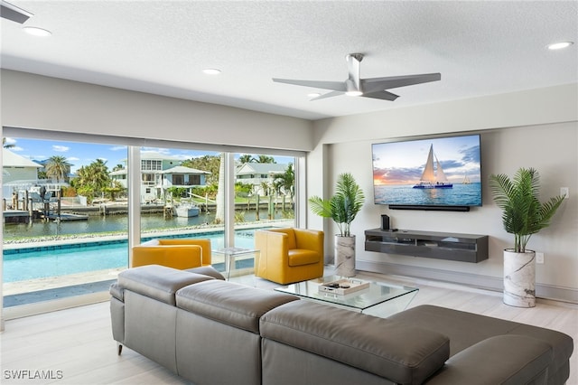 living room featuring a textured ceiling, a water view, light hardwood / wood-style flooring, and ceiling fan