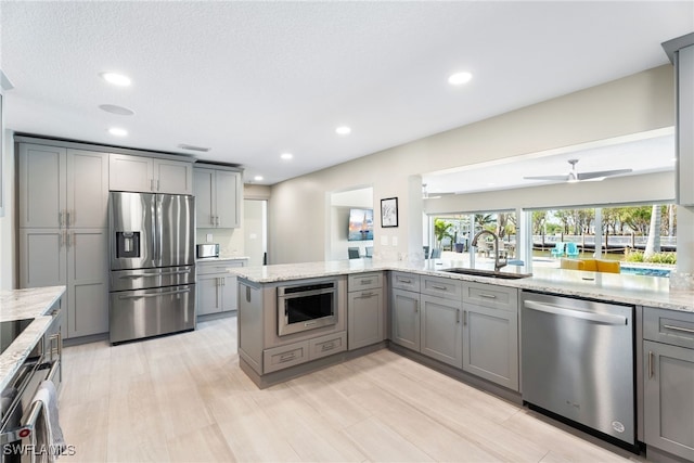 kitchen with light stone countertops, sink, stainless steel appliances, gray cabinets, and light wood-type flooring