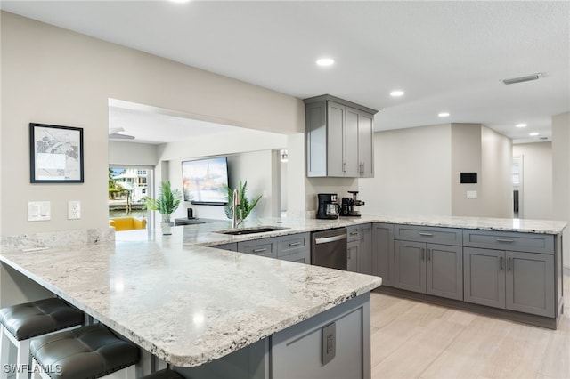 kitchen with gray cabinetry, a breakfast bar, light wood-type flooring, and kitchen peninsula