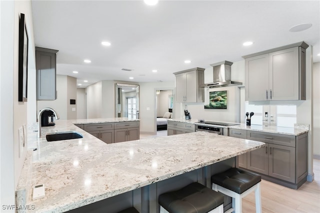 kitchen with kitchen peninsula, light wood-type flooring, a breakfast bar, wall chimney range hood, and sink