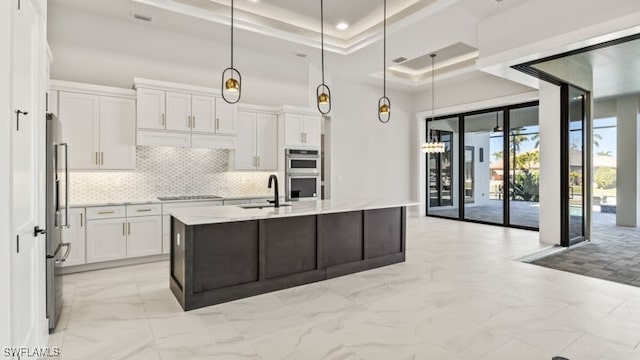 kitchen featuring white cabinetry, a center island with sink, hanging light fixtures, and sink